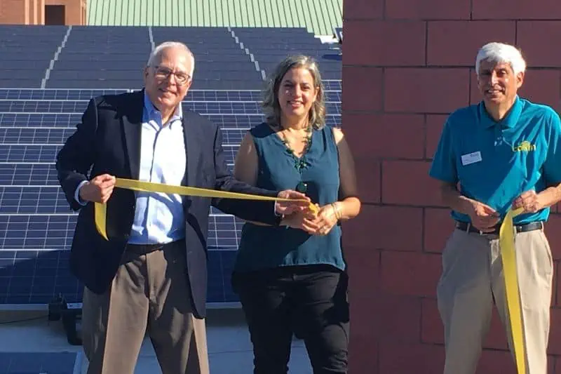 three people at a ribbon cutting ceremony with solar panels behind them