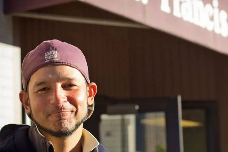 man with a backwards north coast hat smiling outside St Francis Center