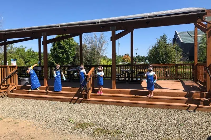 kids standing at a pavilion with long aprons and gloves on