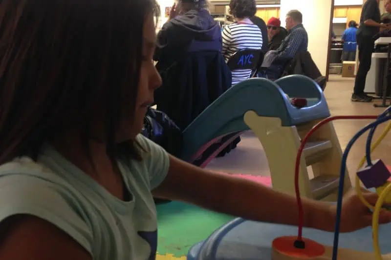 young girl playing at a table with adults sitting behind her