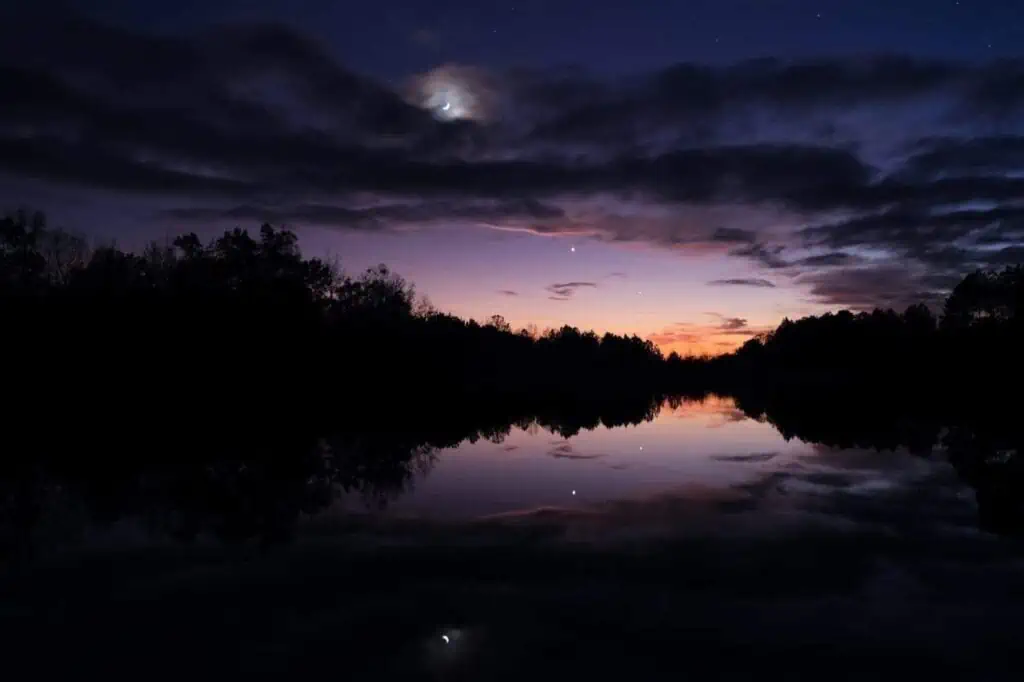 nighttime sky showing purple tones over water and trees