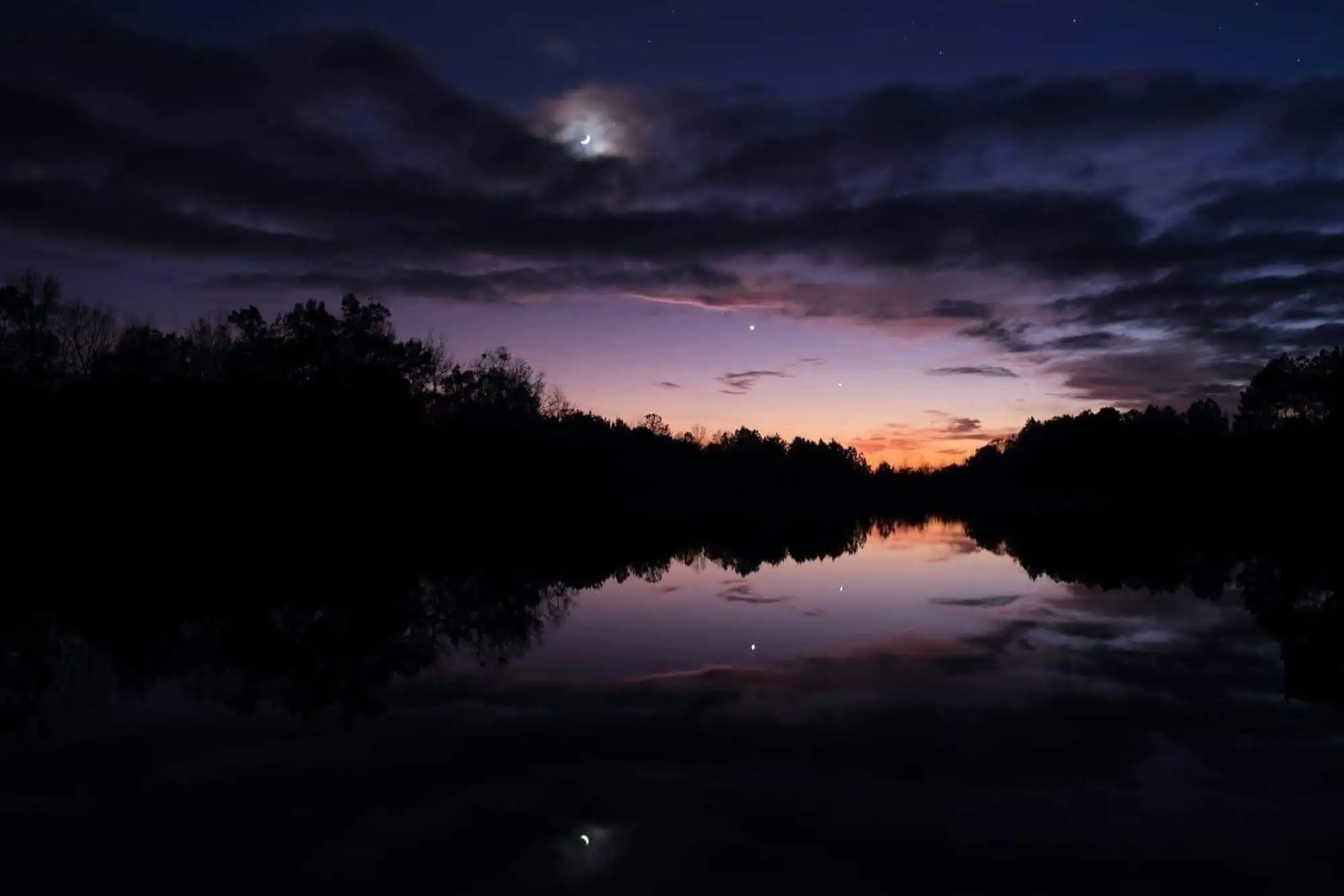 nighttime sky showing purple tones over water and trees