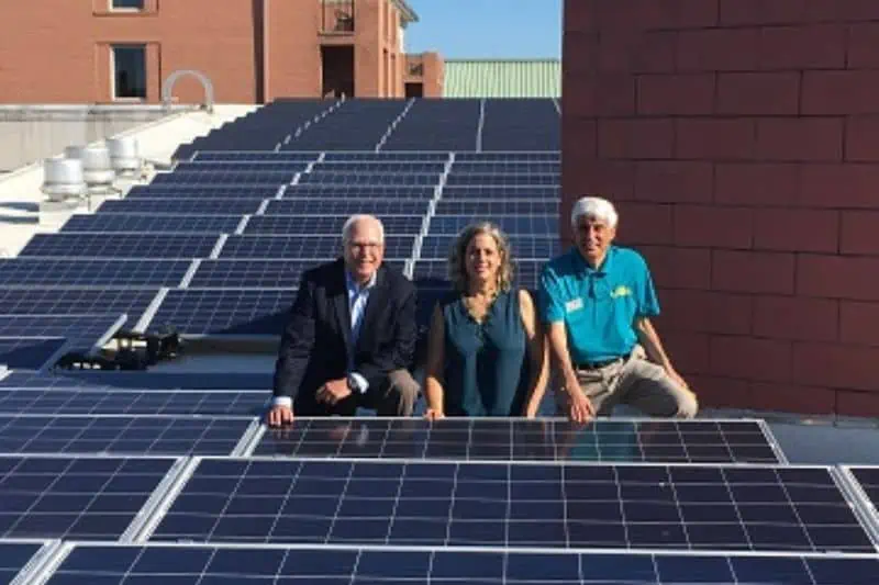 2 men and 1 woman standing by the solar panels installed on a roof