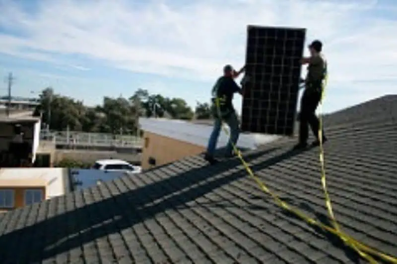 two men carrying a solar panel on a roof