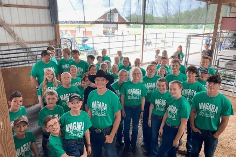 Kids wearing green shirts posing for a picture stand in a barn